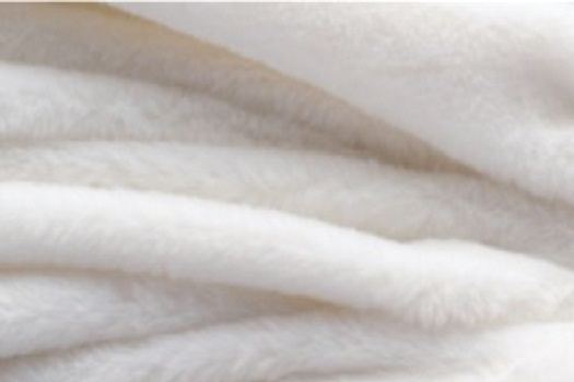Detalle de guata blanca de alto volumen: una masa esponjada de fibra sin superficie lisa, con relieve y sombras suaves entre los mechones