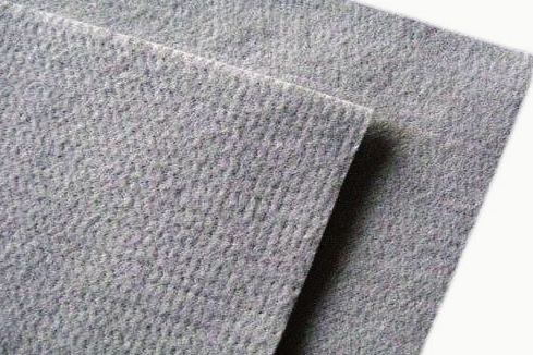 Detalle de tela punzonada gris doblada sobre sí misma: superficie mate y afieltrada, con el picado fino que dejan las agujas y el canto de la doblez a la vista