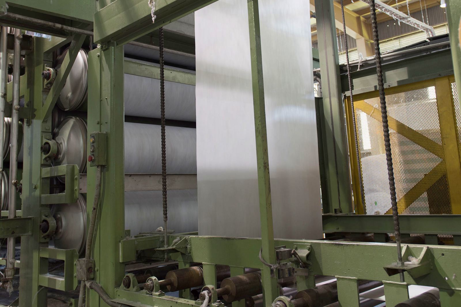 Línea de producción de tela no tejida: el velo blanco avanza a lo ancho entre los rodillos y tambores de la máquina
