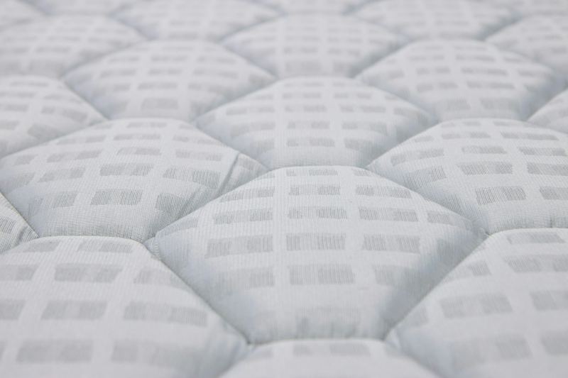Macro de la superficie de un colchón blanco: celdas acolchadas en relieve formadas por el pespunte sobre el relleno