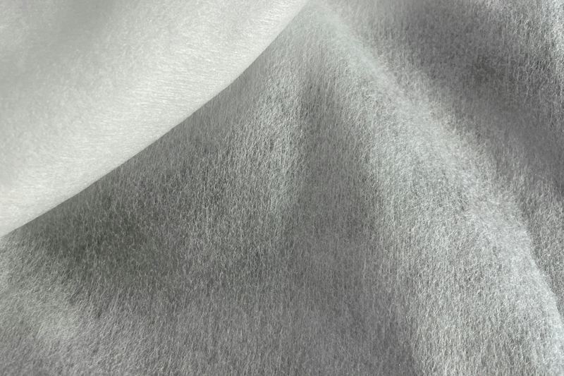Macro de un no tejido suave blanco y gris, con la trama de fibras dispersas típica del spunlace y sin ningún patrón de tejido visible