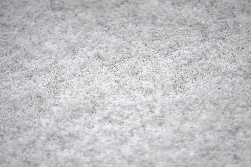 Primer plano de una superficie textil gris claro de aspecto afieltrado, con las fibras entrelazadas en tonos blanco y gris